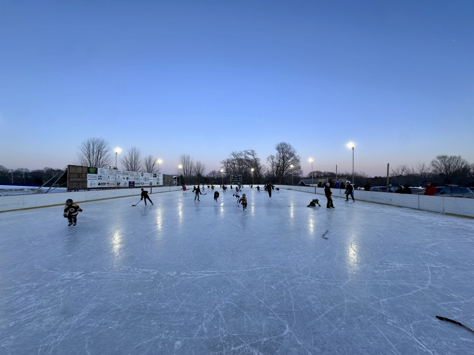 A full sheet of skaters at an evening open skate, with sponsor banners lining the boards